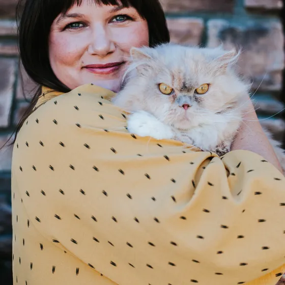 Dr. Sarah Bason holding a fluffy Persian cat against the practice's exterior stone wall.